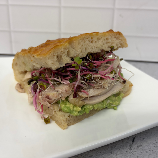Focaccia sandwich with zesty guacamole, chicken, sprouts, greens + mayo on housemade focaccia